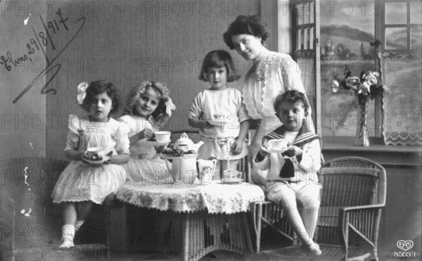 Mother with children around a coffee table, 1920s, Four children and a woman enjoying a tea party