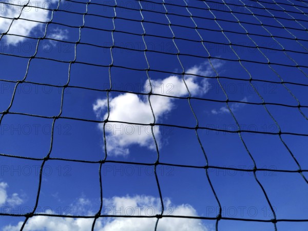 Looking up at a blue sky filled with clouds, framed by a black net. The sunlight highlights the