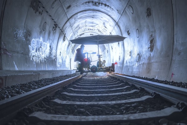 An illuminated tunnel with rails and graffiti on the walls. In the background is a figure with a