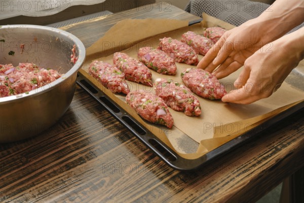 Hands shape meat patties on a lined baking tray in a warm kitchen. This preparation hints at a