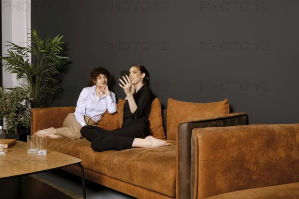Two friends are seated comfortably on a brown couch in a modern living room. They are engrossed in