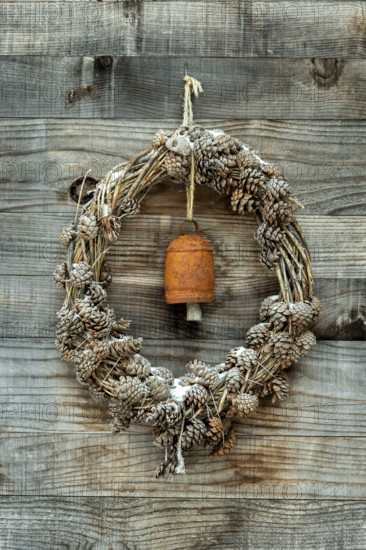 A wreath made of pinecones and natural materials is displayed on a rustic wooden wall. An antique