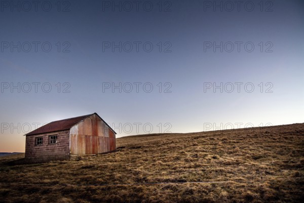 An isolated wooden hut sits on a grassy slope in the Regional Nature Park of Volcans d'Auvergne,