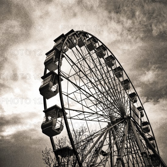 A towering Ferris wheel emerges against a swirling, moody sky during twilight hours, evoking