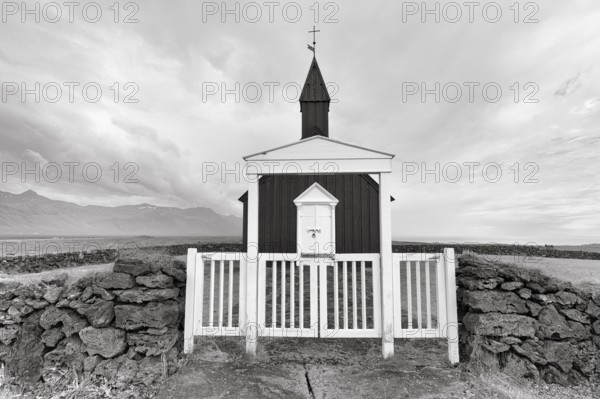 Traditional black church with white wooden door and stone wall, wooden church Budakirkja,