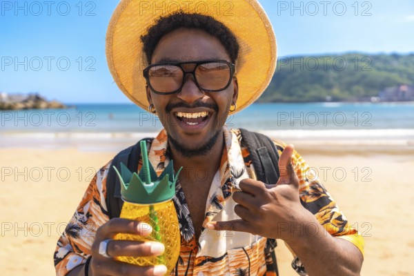 Young man enjoying summer vacation on a tropical beach, holding a pineapple shaped cocktail and