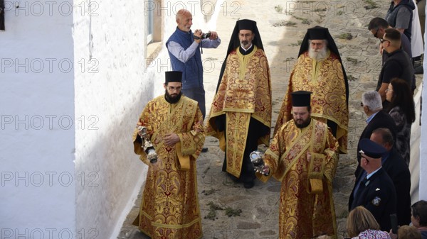 Clerics in richly decorated robes walk along a stone alley, spectators take photos, Orthodox