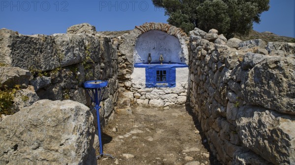 Small stone chapel with blue façade embedded in ancient ruins under a bright blue sky, Artemis