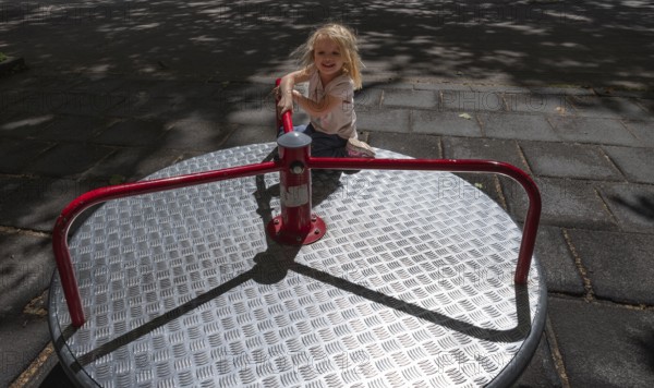 Outdoor shot, little girl, 3 years old, blonde, playing on a merry-go-round, children's playground,