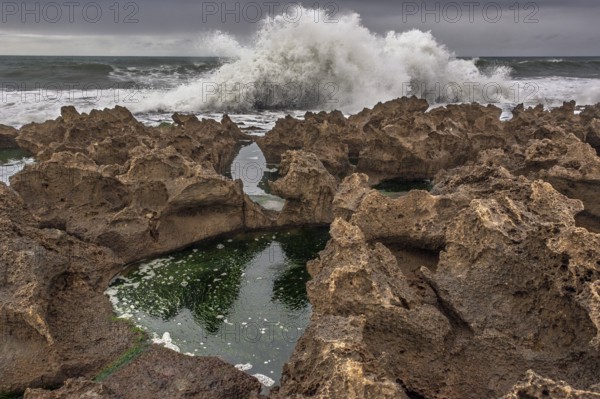 A rocky area with a hole in the ground. The hole is filled with water. The water is brown in colour