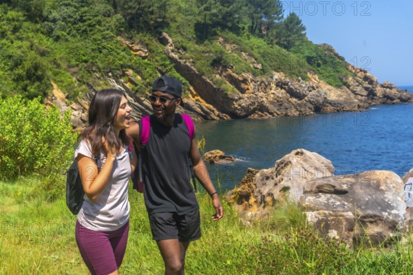 Young couple walking and laughing along a beautiful coastline path on a sunny summer day, enjoying