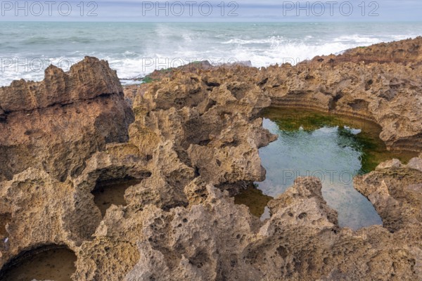 A rocky area with a hole in the ground. The hole is filled with water. The water is brown in colour