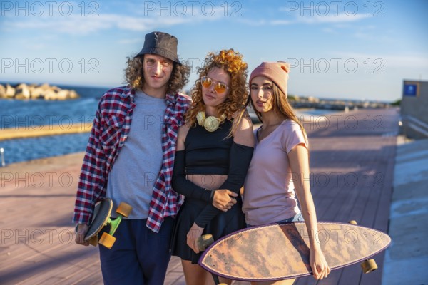 Three friends with skateboards relax by the seaside, enjoying the sunny weather and casual outdoor