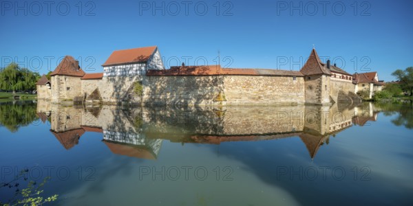The town wall with defence towers and half-timbered house is reflected in the lake pond,