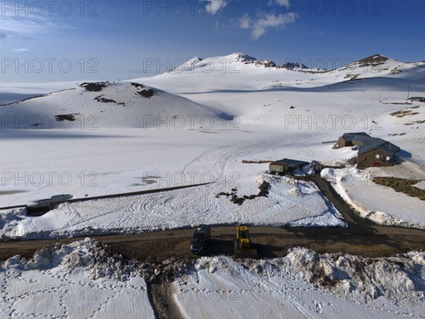 Huts and a road embedded in snow-covered mountains under a clear blue sky, aerial view, Aragaz,