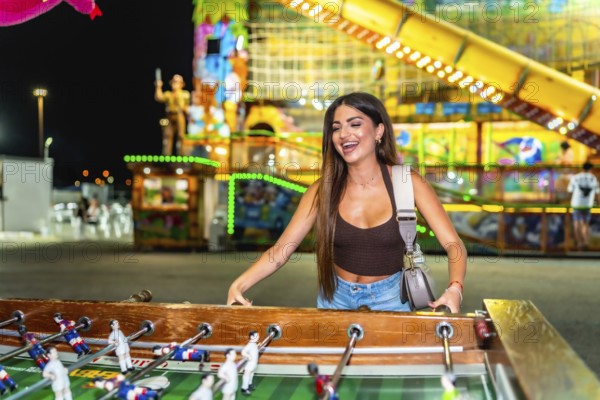 Happy young woman enjoying a vibrant evening at a funfair, playing table football and soaking up