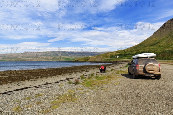 Tourist enjoying solitude in fjord landscape, SUV with roof tent, Skápadalur valley, coastline,