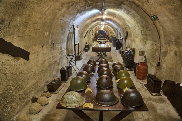 A tunnel with a row of helmets on a table, in the background exhibits, steel helmets, war museum,