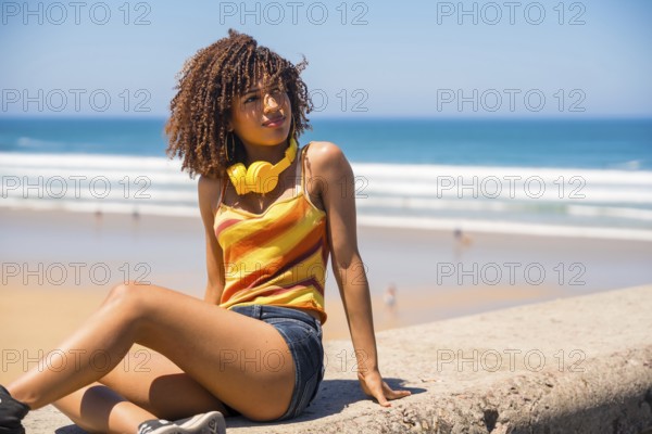 Young woman with headphones relaxing on beach wall enjoying summer vacation, looking away from