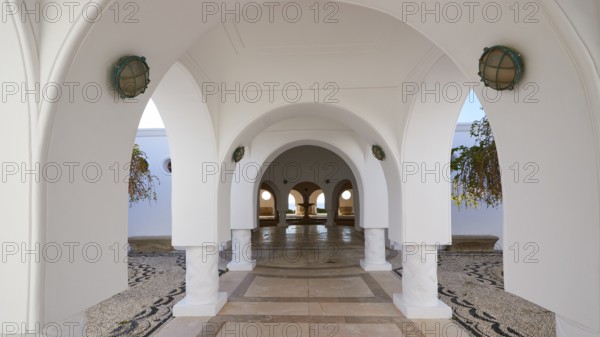 A tranquil area with white arches and hanging plants, framed by decorative arches and lights,