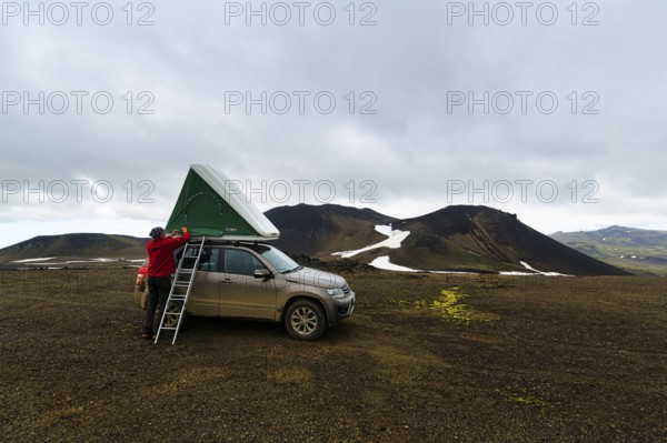 Barren volcanic landscape with snowfields, off-road vehicle with roof tent and ladder on mountain