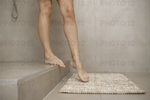 A person is carefully stepping out of a sleek shower onto a plush bath mat in a contemporary