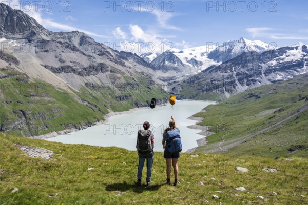 Two female friends throw their hats in the air, female mountaineers in front of a blue mountain