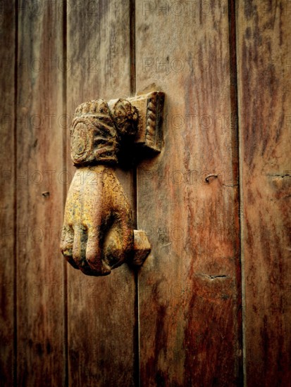 A vintage hand-shaped door knocker is mounted on a weathered wooden door, showcasing intricate