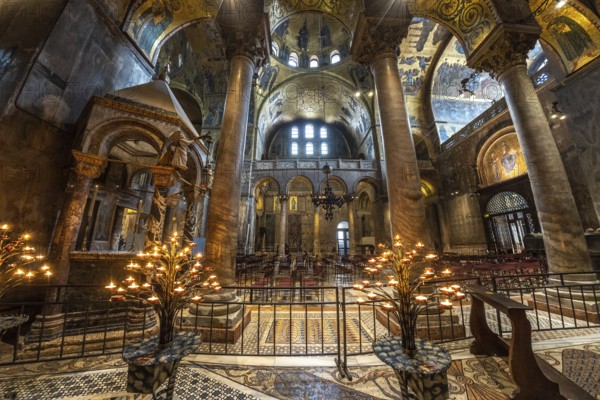 Lit candelabras illuminate the mosaic decorations and marble columns inside saint mark's basilica
