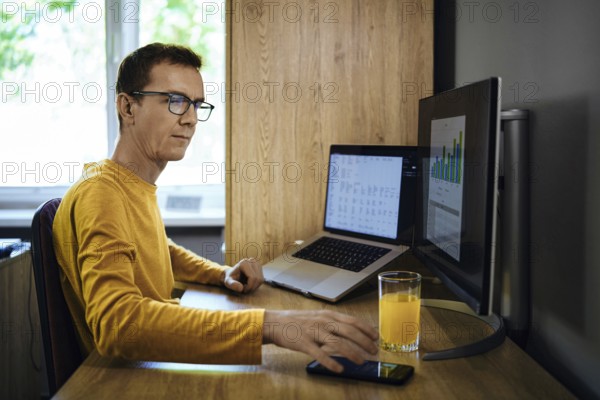 A man in a yellow shirt sits at a desk in a home office. He was distracted from studying statistics