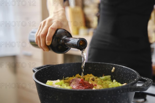 A hand pours liquid into a pot filled with chopped vegetables and sauce, creating a delicious