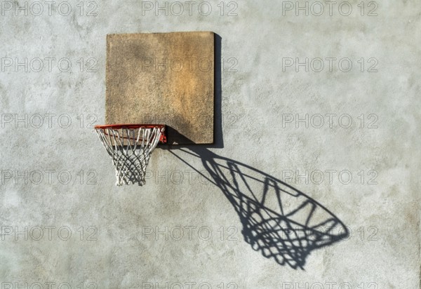 A worn basketball hoop is mounted on a textured wall, with the sunlight creating a captivating