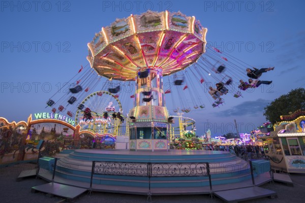 Colourfully illuminated carousel at a funfair in front of a night sky, chain carousel, spring
