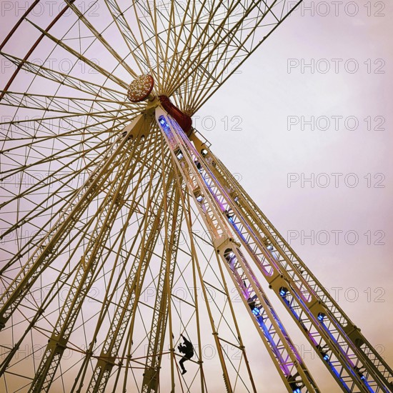 A maintenance worker is seen climbing the structure of a ferris wheel that features vibrant lights.