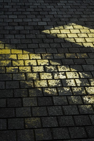 Faded yellow markings on dark, textured stone pavement create a striking contrast. The uneven