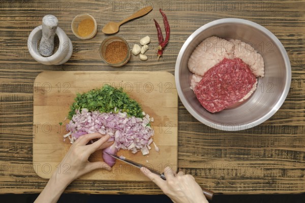 Hands chop shallots and parsley on a wooden cutting board. Ground meat is prepared in a bowl