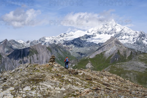 Female mountaineer on hiking trail with cairn, behind glaciated and snow-covered summit of the