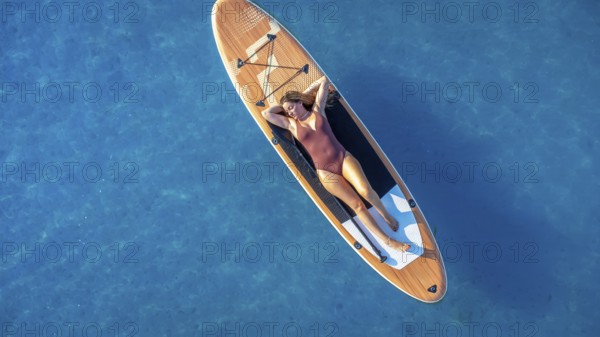 Lying on a paddle board, a woman enjoys the tranquility of the calm blue sea, soaking up the sun
