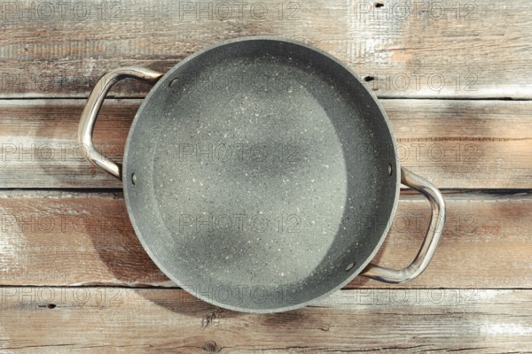 A gray frying pan with two sturdy handles on a weathered wooden tabletop. The pan is designed for