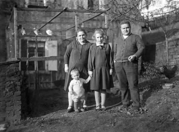 Family in front of a birdcage, 1930s, Family of four standing in a rural garden area, all looking