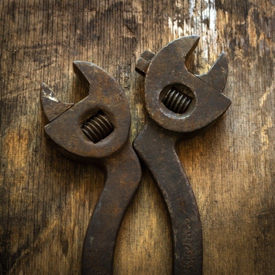 Two vintage adjustable wrenches lie side by side on a textured wooden surface, showing signs of
