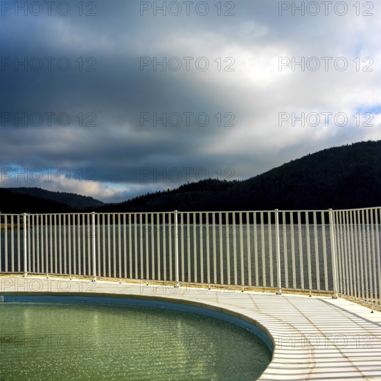 A serene lake reflects the overcast sky, with gentle ripples on the surface. Fencing outlines the