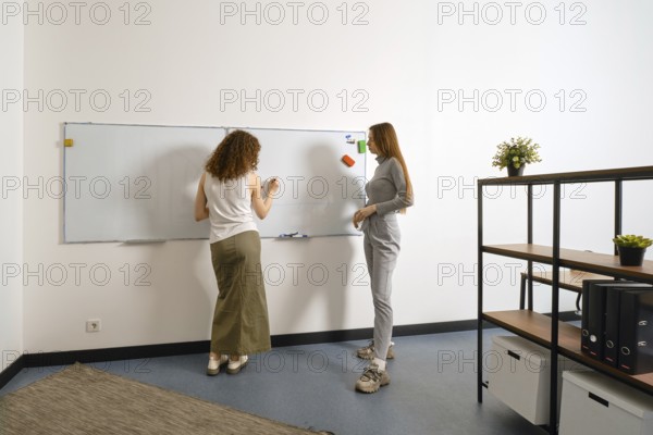 Two women collaborate on a whiteboard in a bright office dedicated to women's health. They discuss