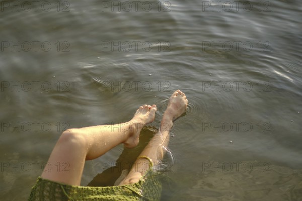 On a sunny day at the lake, a person enjoys the cool water, dipping her feet in while seated