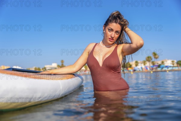 Young woman wearing swimsuit posing in the sea next to her paddle board, enjoying summer vacation