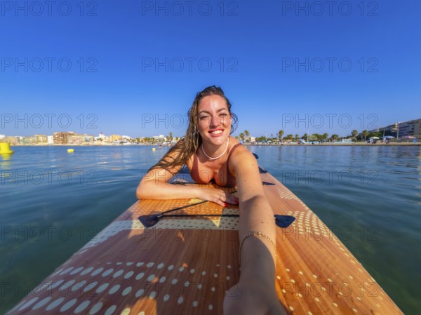 Young woman lying on a paddle board, soaking up the sun and enjoying a relaxing summer vacation by
