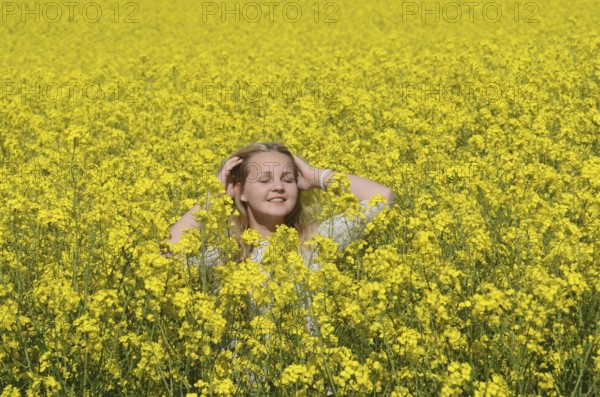 Blonde girl, 15 years old, stands smilingly in flowering rapeseed field in Ystad Municipality,