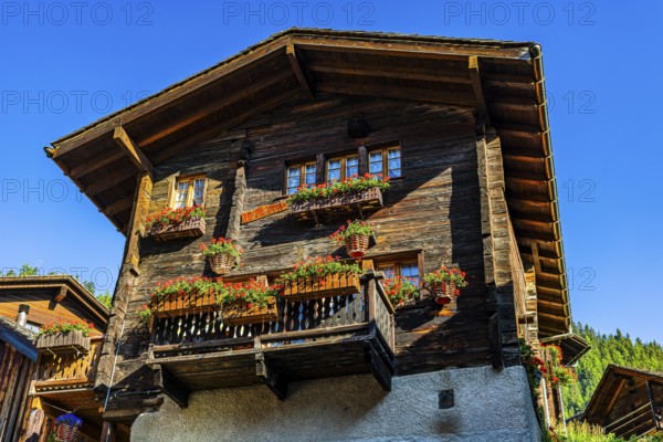 Old wooden house in log construction, decorated with flowers, historic village centre, Grimentz,