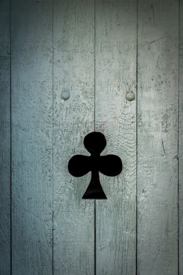 A black club symbol is prominently displayed on a weathered blue wooden door. The door's texture
