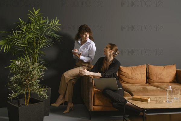 Two women engage in a lively discussion in a contemporary office. One holds a notepad while sitting